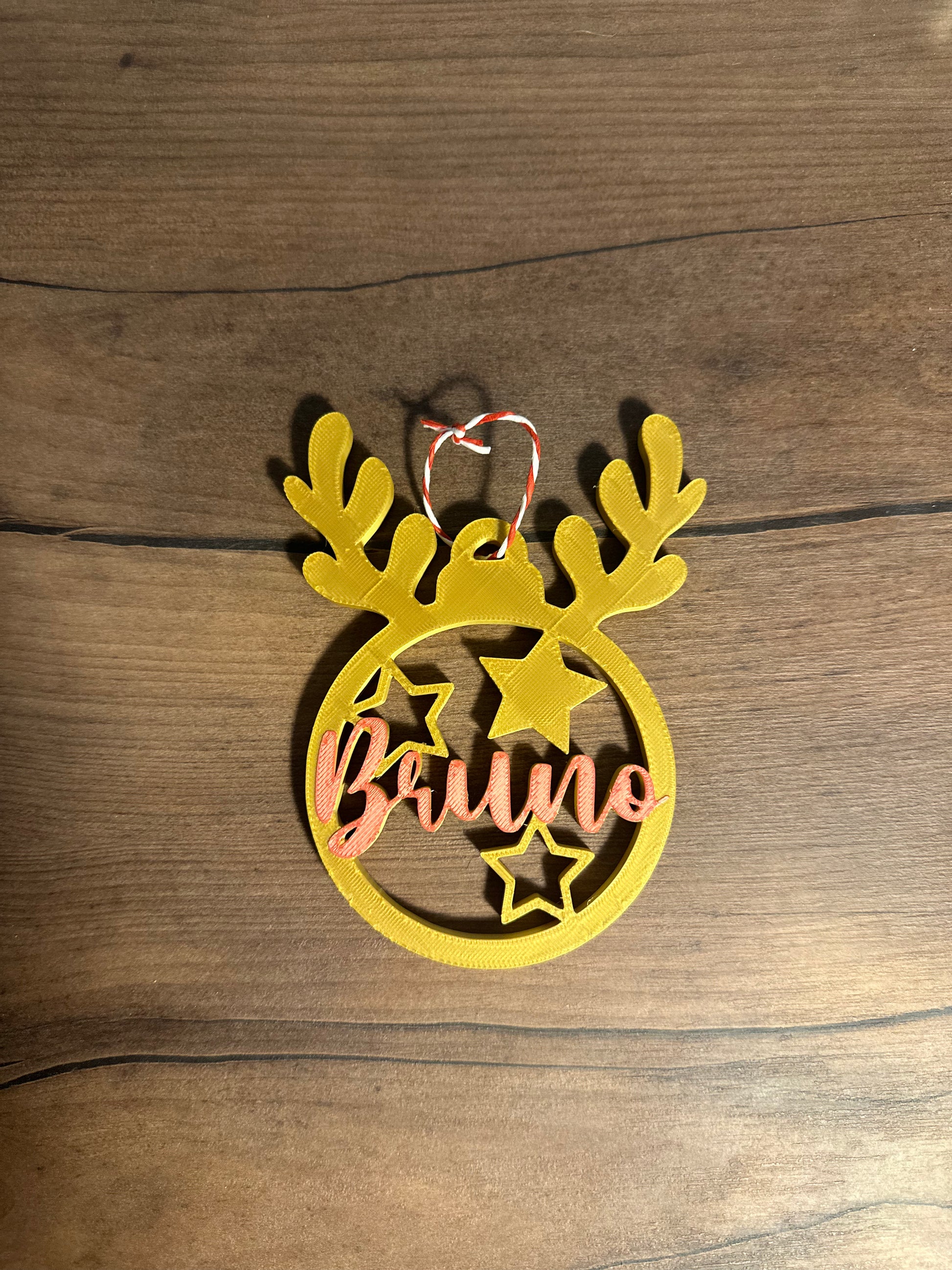 Bola de navidad en forma de reno personalizable impreso en 3d de color amarillo y el nombre de bruno en rojo
